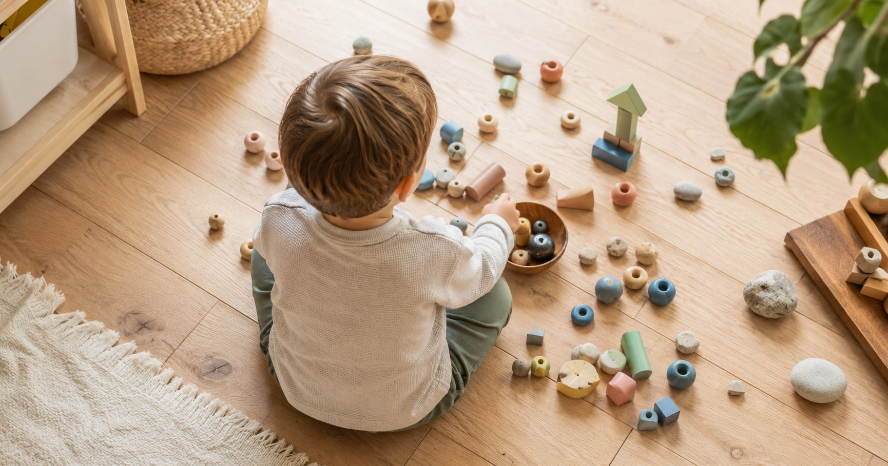 Kind beim Spielen mit kleinen bunten Spielzeugteilen und Holzperlen auf einem hellen Holzboden — symbolisch für das Neugierverhalten von Kleinkindern