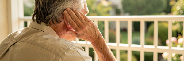 Älterer Mann auf sonniger Terrasse lauscht aufmerksam — Symbol für nachlassendes Hörvermögen