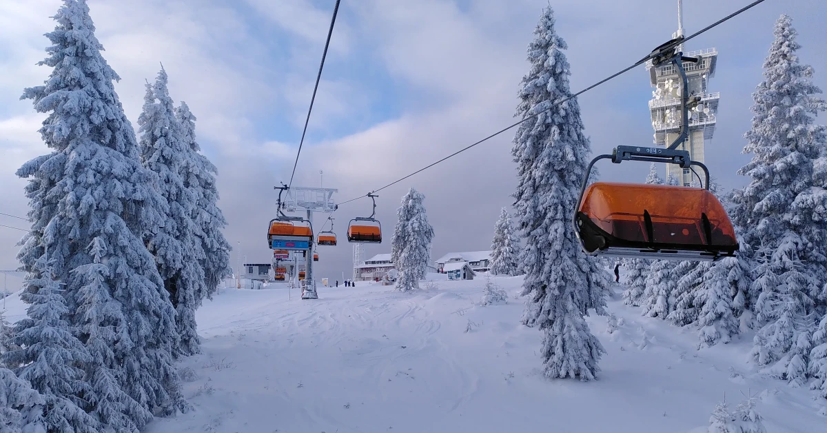  Verschneiter Berg aus Sicht eines Sessellifts, umrahmt von schneebedeckten Bäumen, bewölkter Himmel, eisige Winterluft.
