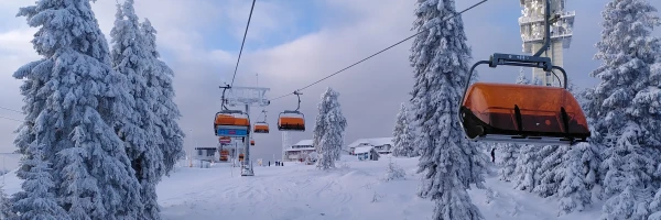  Verschneiter Berg aus Sicht eines Sessellifts, umrahmt von schneebedeckten Bäumen, bewölkter Himmel, eisige Winterluft.