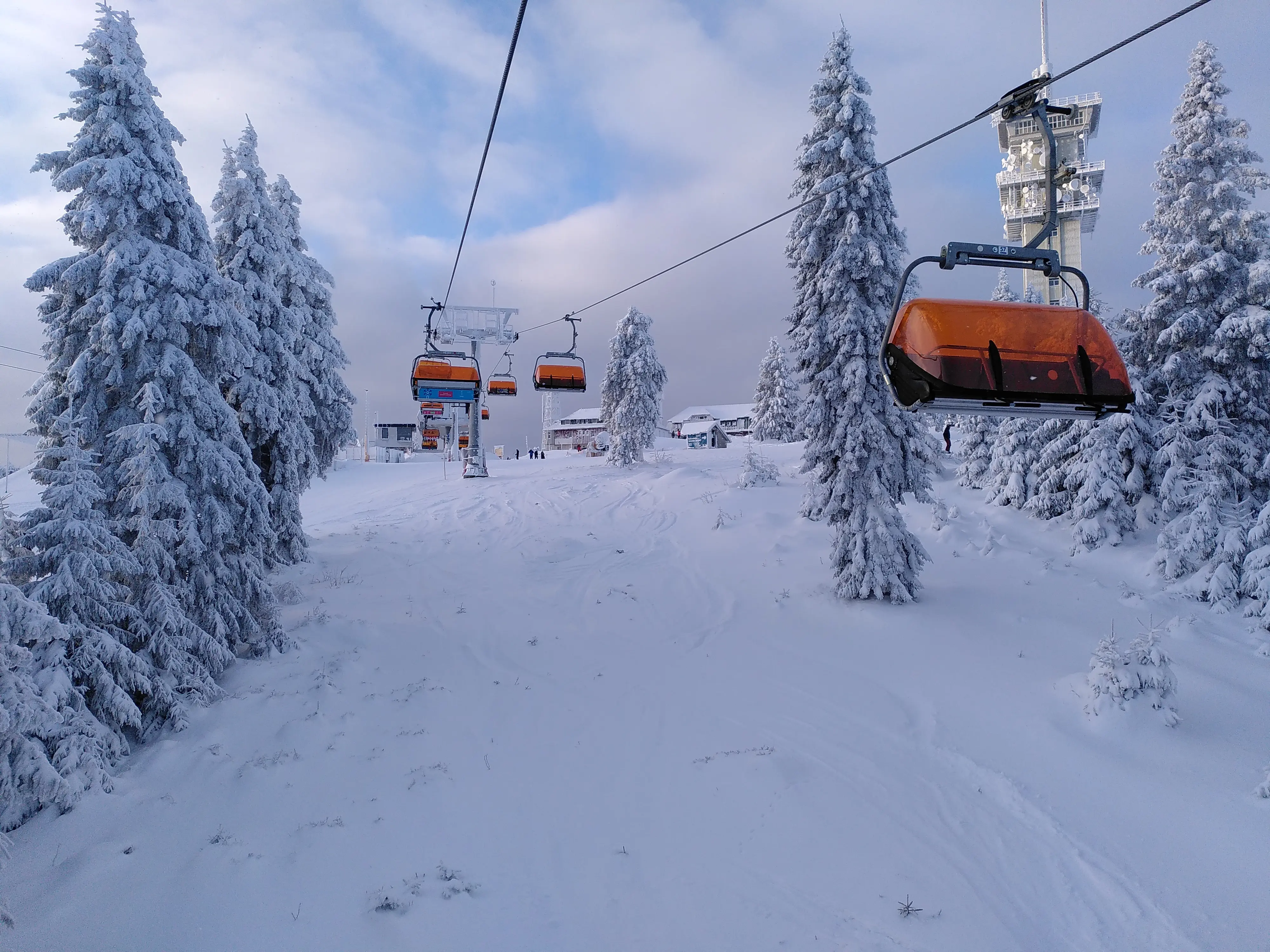  Verschneiter Berg aus Sicht eines Sessellifts, umrahmt von schneebedeckten Bäumen, bewölkter Himmel, eisige Winterluft.